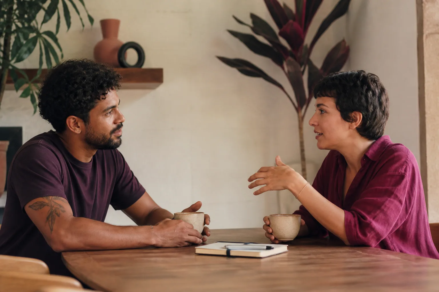 Duas pessoas adultas conversam frente a frente, com a mesma presença visual, em torno de uma mesa.